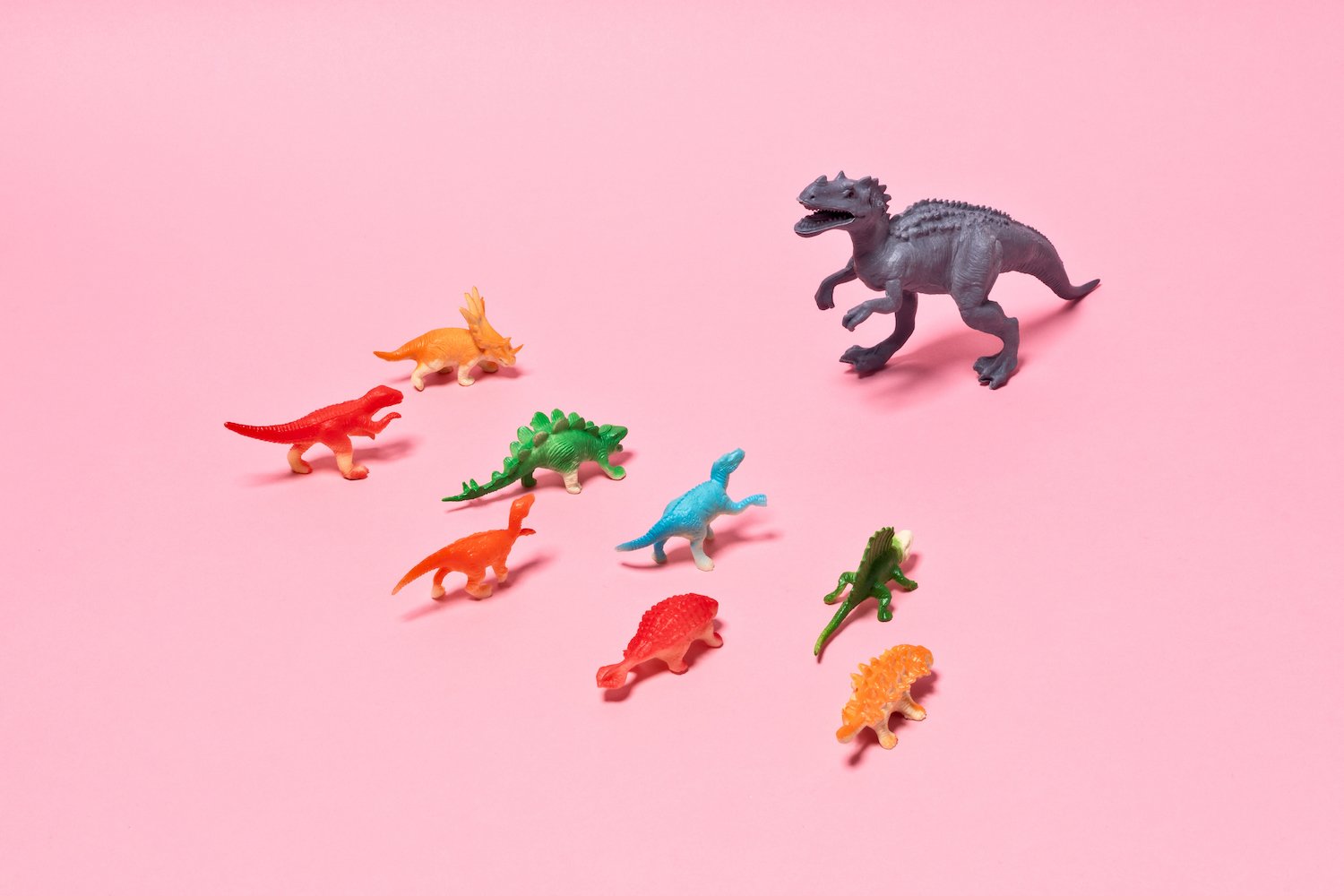 Toy dinosaurs conflict, Rex dinosaur standing out from the crowd on pink background.