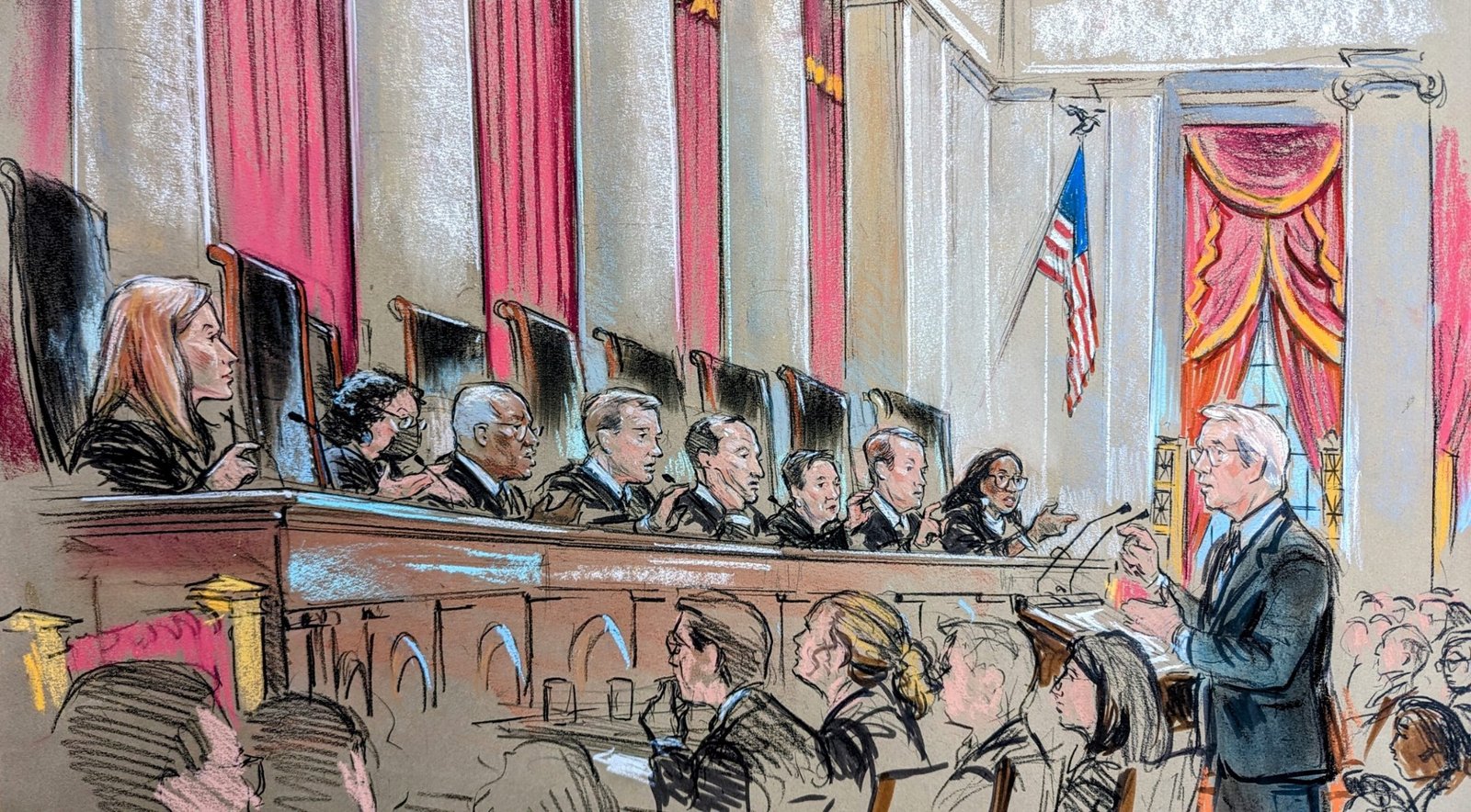 A man speaks at a conference in front of nine bench judges who all appear to be asking him a question.